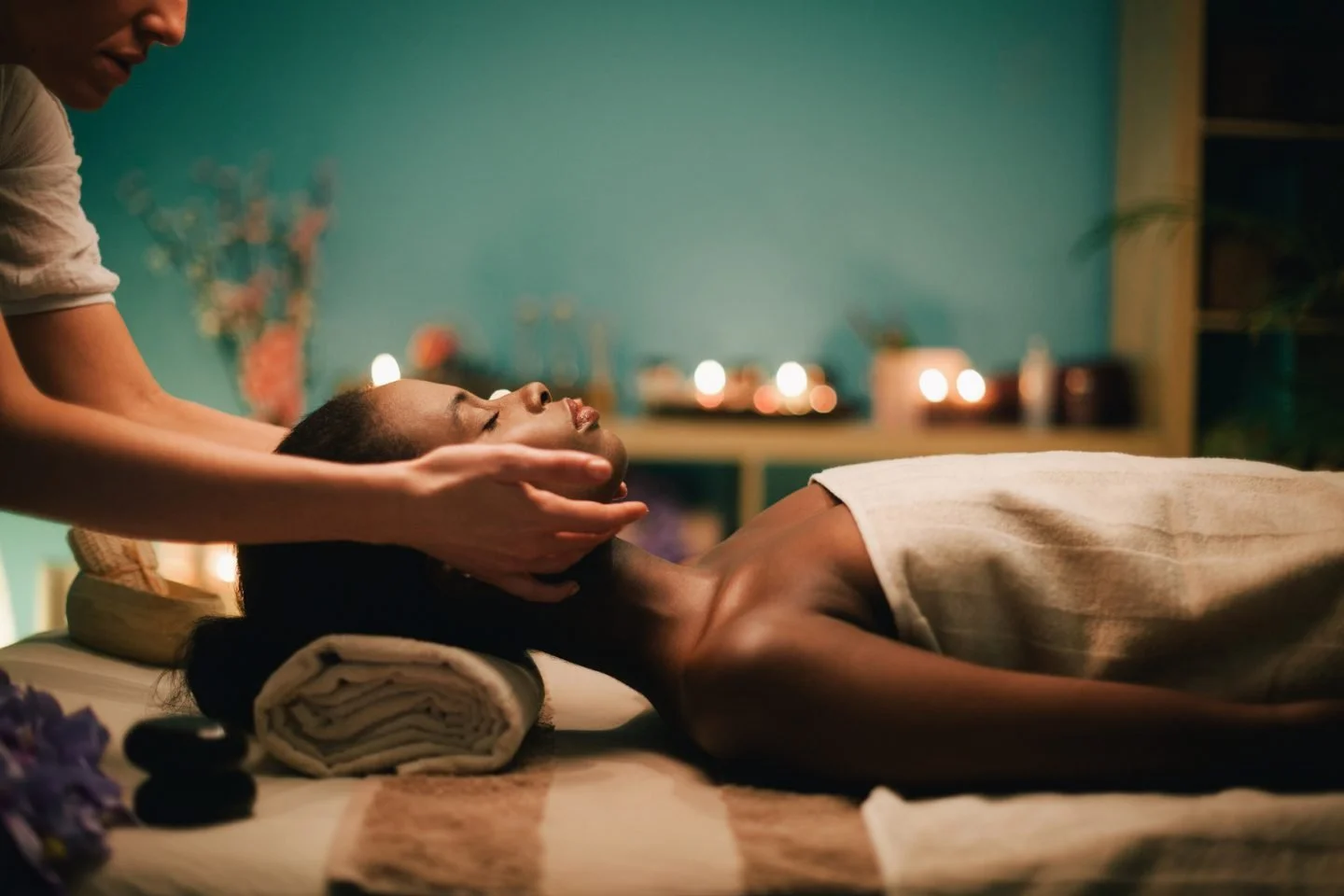 Person receiving a massage in a dimly lit room with candles and decorative items in the background.