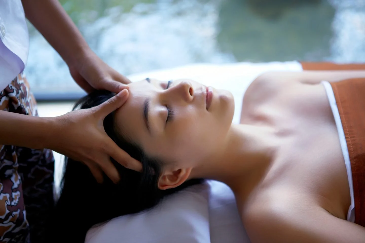 Woman receiving a head massage or facial treatment while lying on a treatment bed.