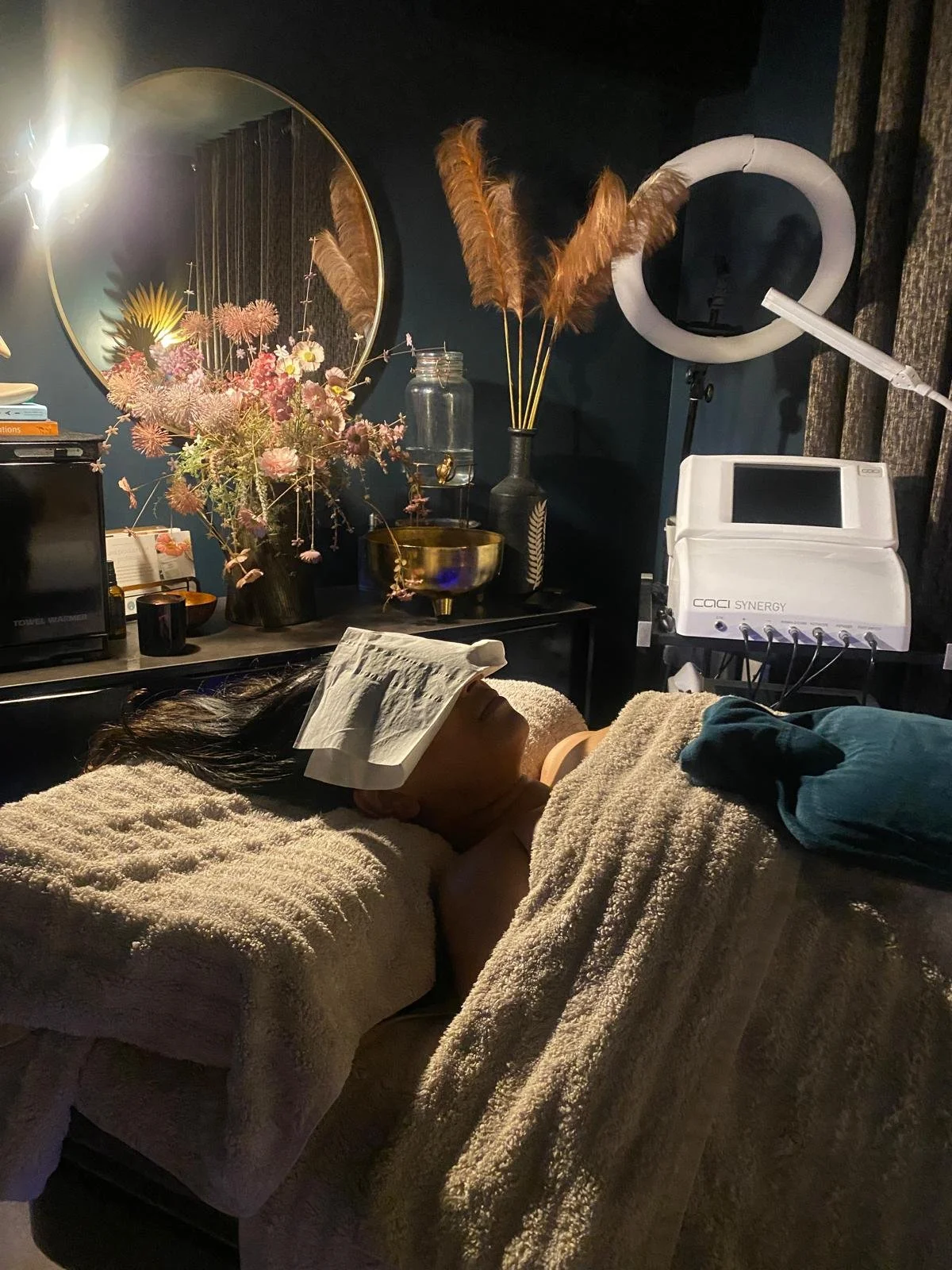 Spa setting with rolled white towels, purple flowers, candles, and stones for relaxation.