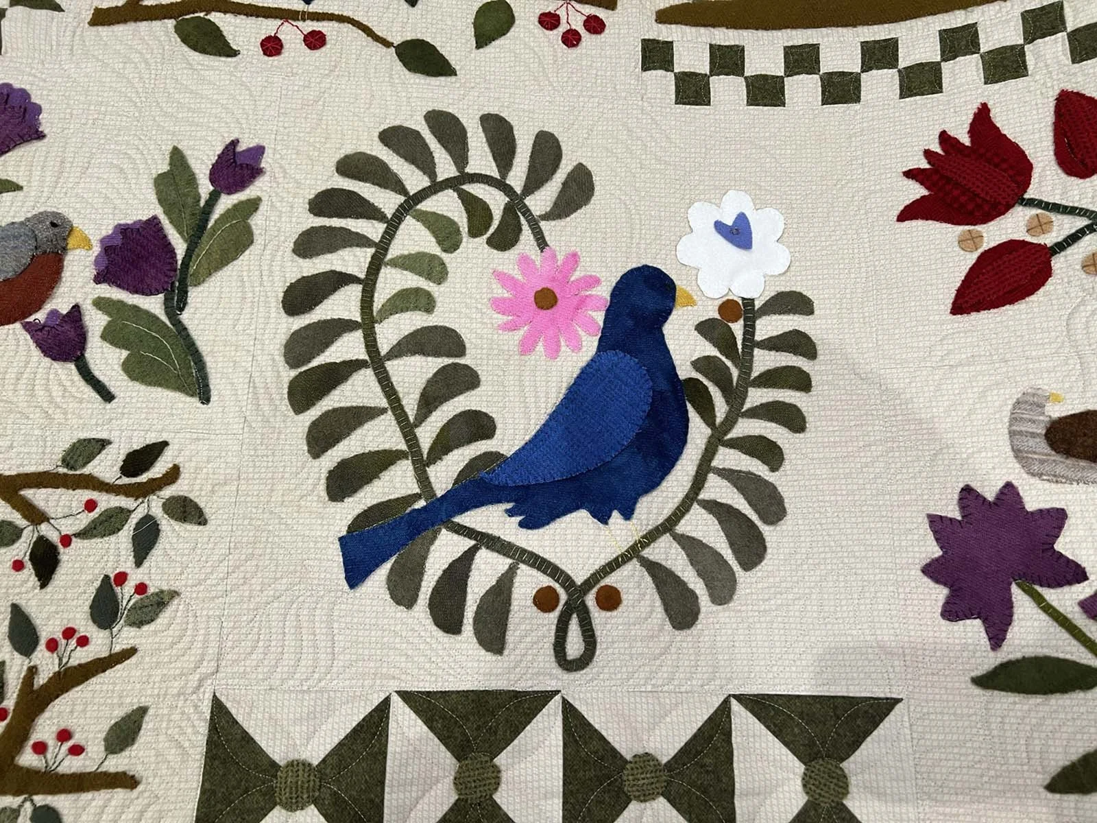 A quilt with an embroidered design of a blue bird sitting on a branch.