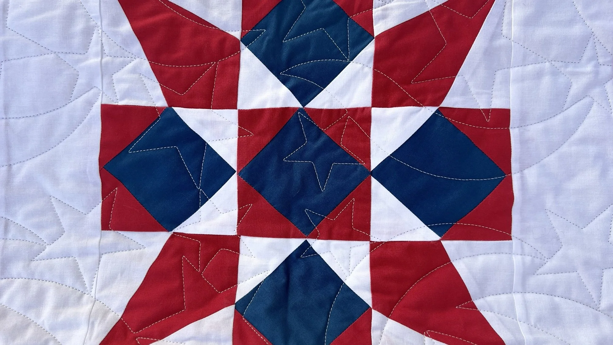 A quilt with a patriotic red, white, and blue star pattern, featuring stitched stars and geometric shapes.