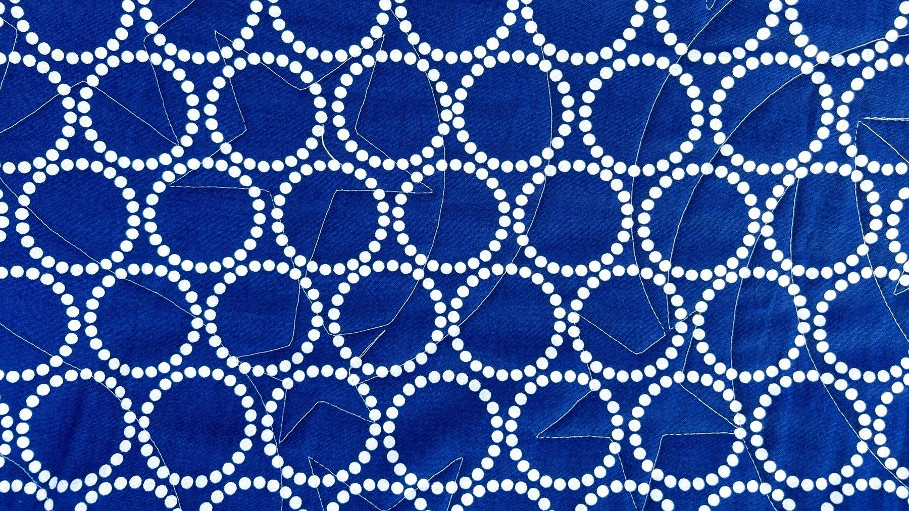 A quilt with a blue background featuring a pattern of white dotted circles connected by lines.