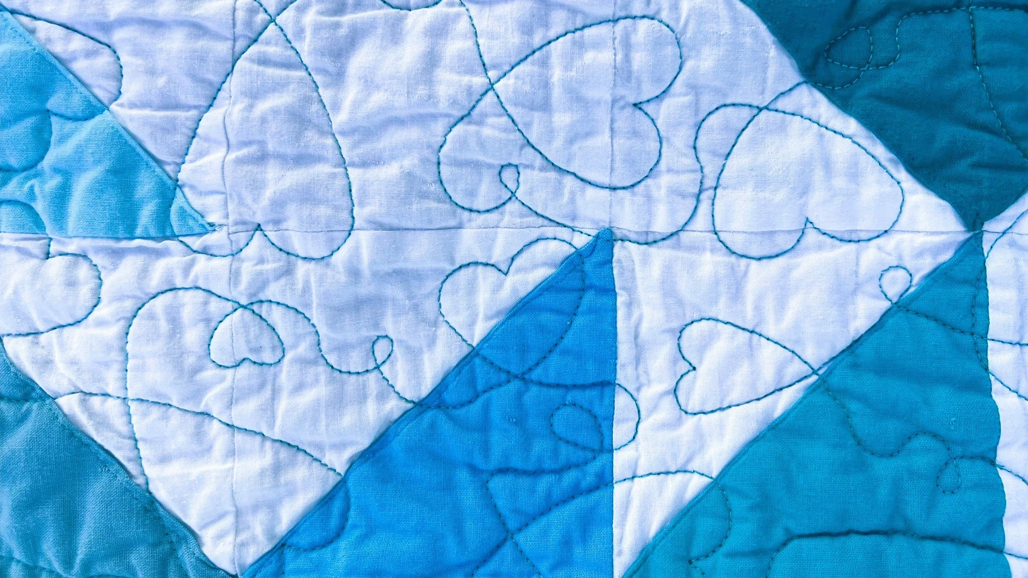 Close-up of a quilt with a pattern of hearts and swirling lines in shades of blue and white.