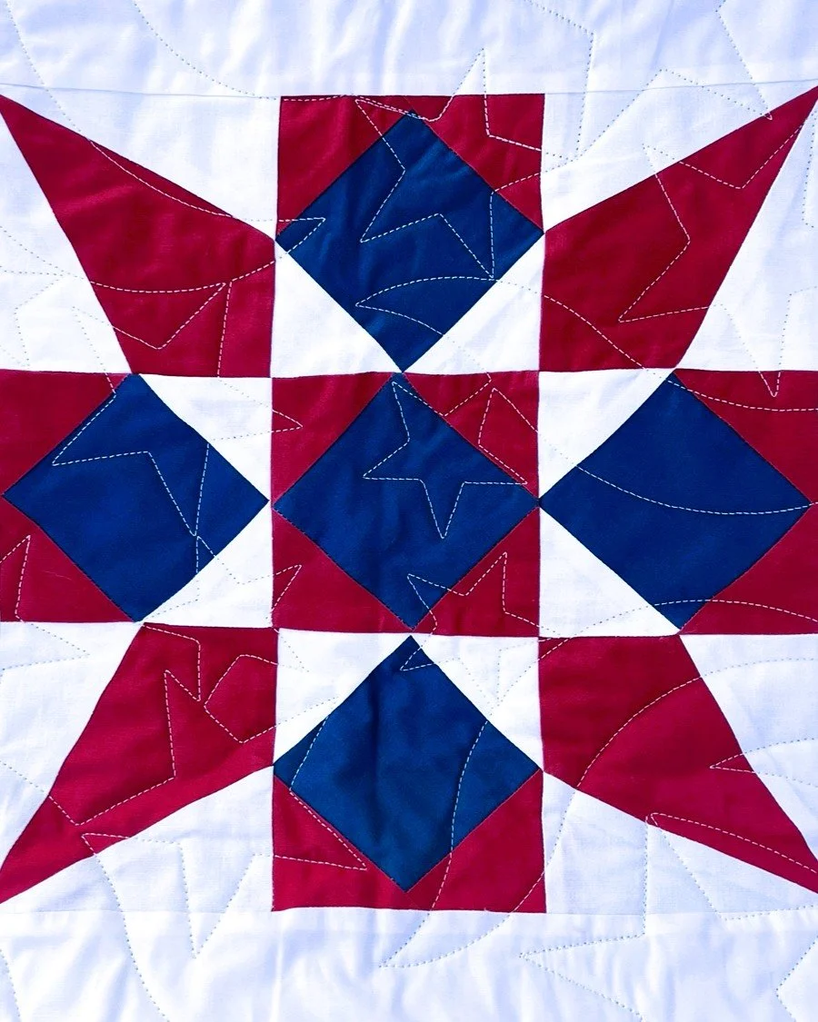 A quilt with a patriotic star pattern in red, white, and blue colors, featuring embroidered outlines of stars.
