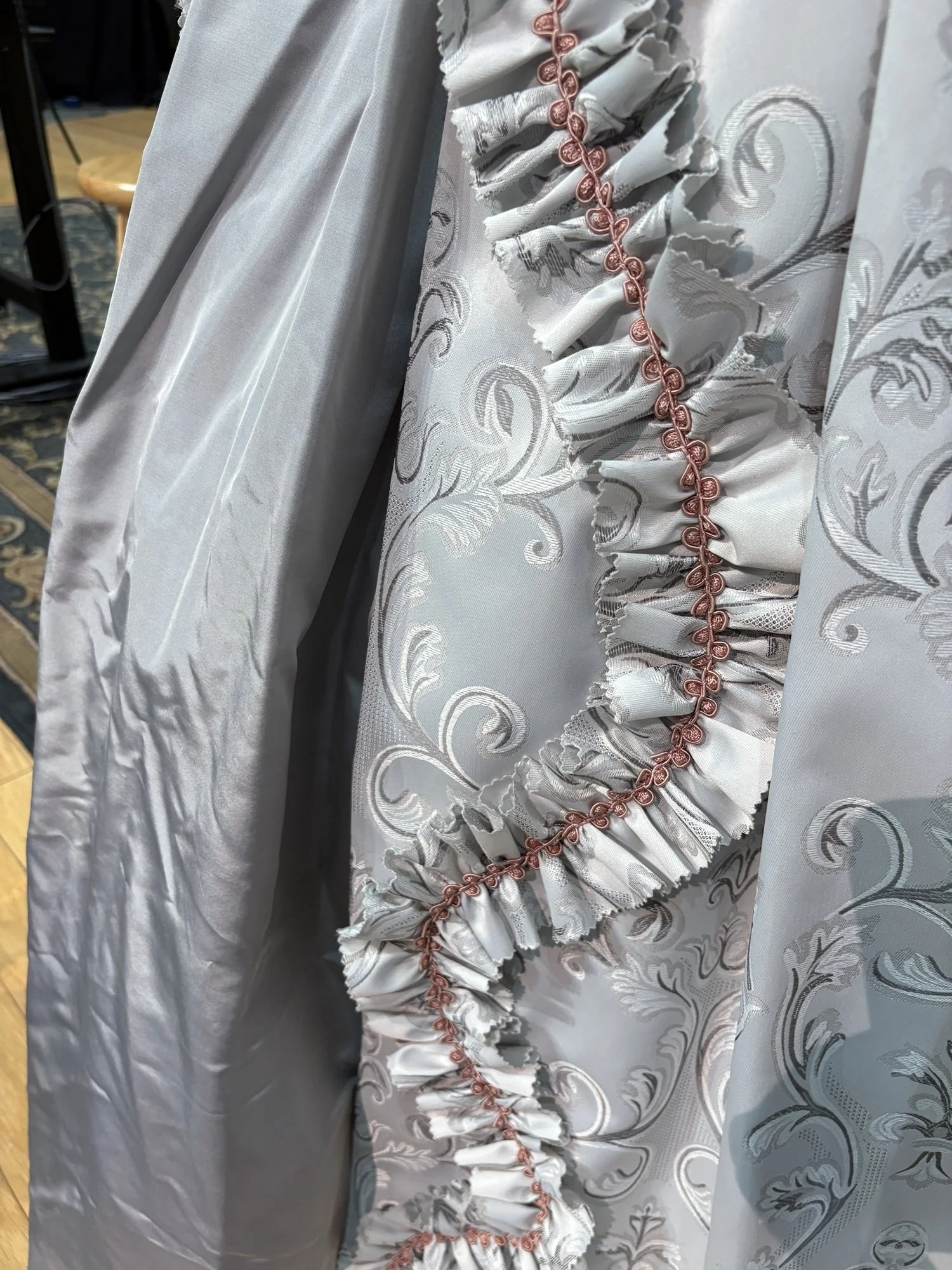 Ruffled trim and ornate fabric patterns highlight the gown’s layered textures, adding movement and theatrical flair to the design.
