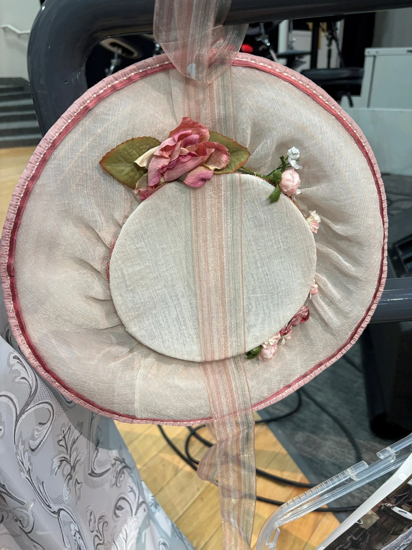 Coordinating period hat with soft ribbon and floral accents, completing the dramatic wedding ensemble.