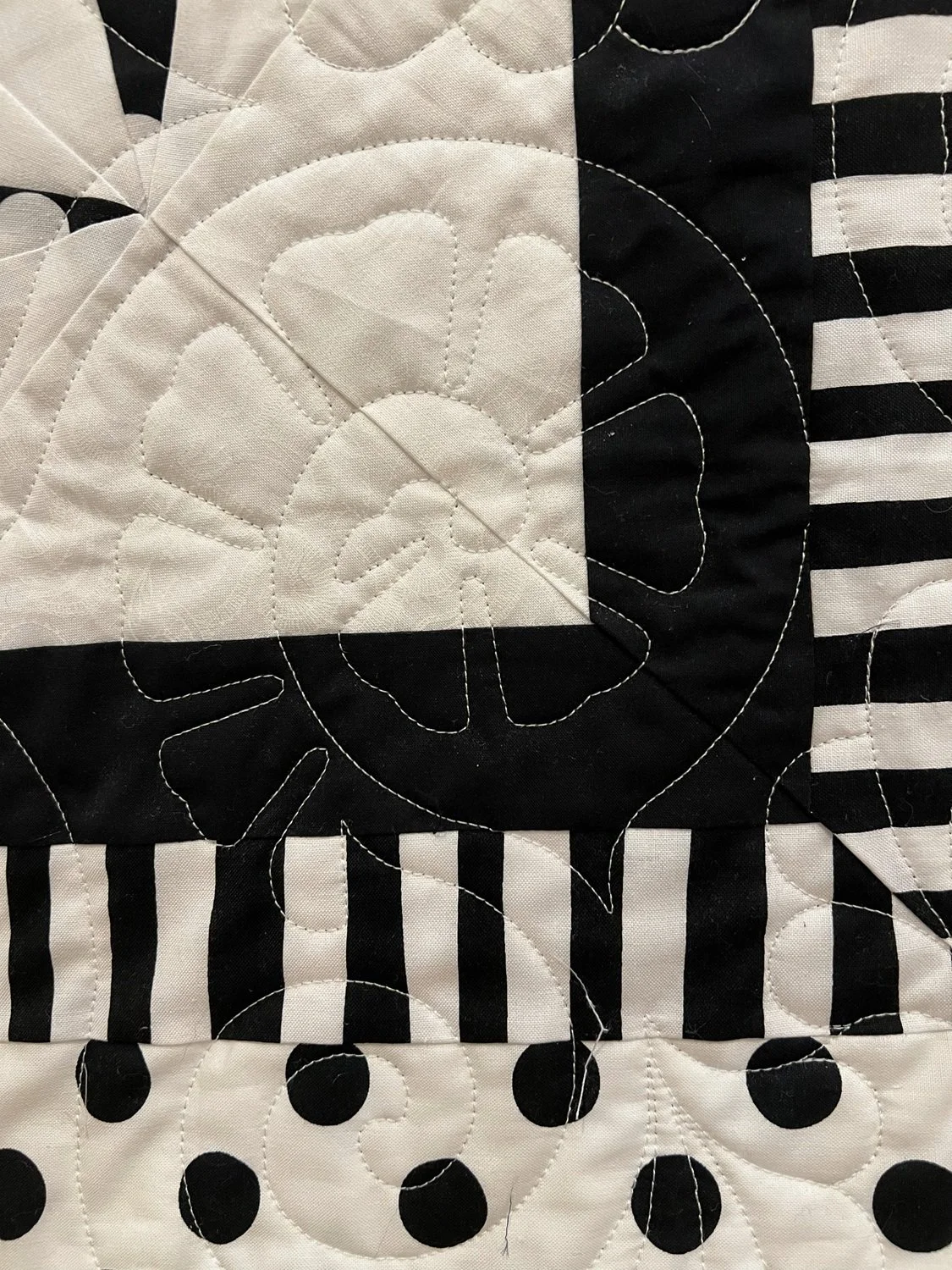 Close-up of a black and white quilt with stitched fabric, featuring a skull and polka dot pattern.