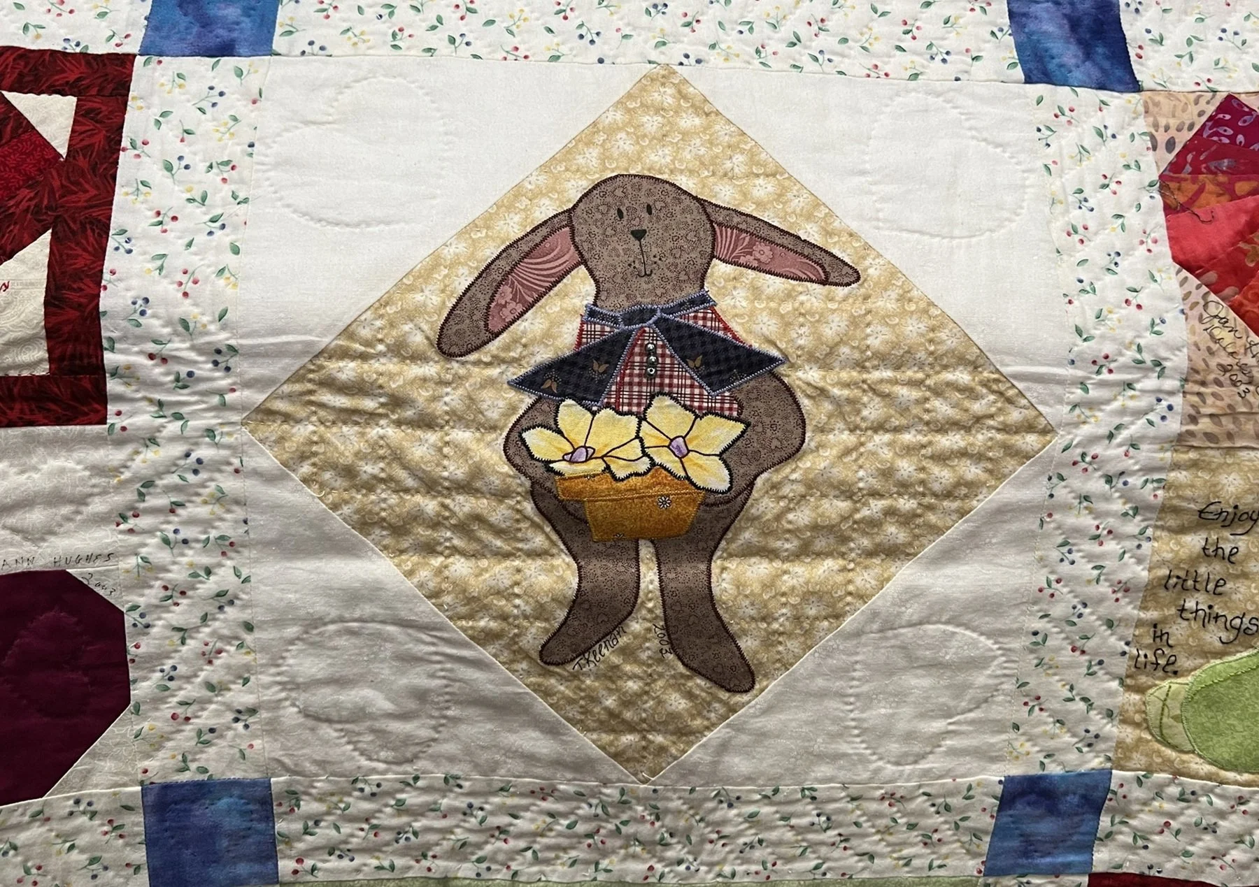 A quilt with a central embroidered image of a bunny holding a basket with yellow flowers.