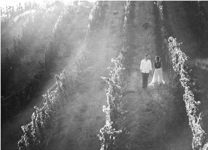 A man and woman walking together in a vineyard during sunlight.