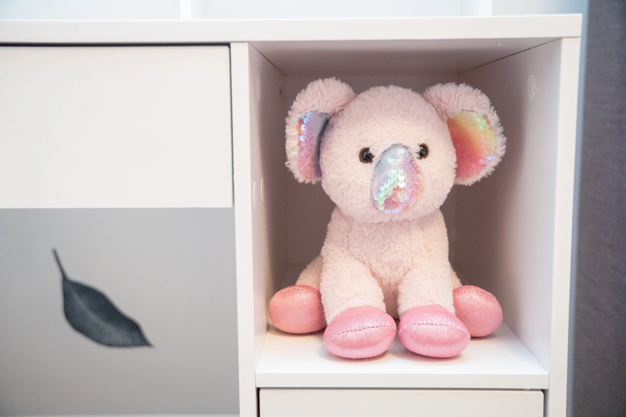 Pink plush teddy bear with sequined snout and ears sitting on a white shelf