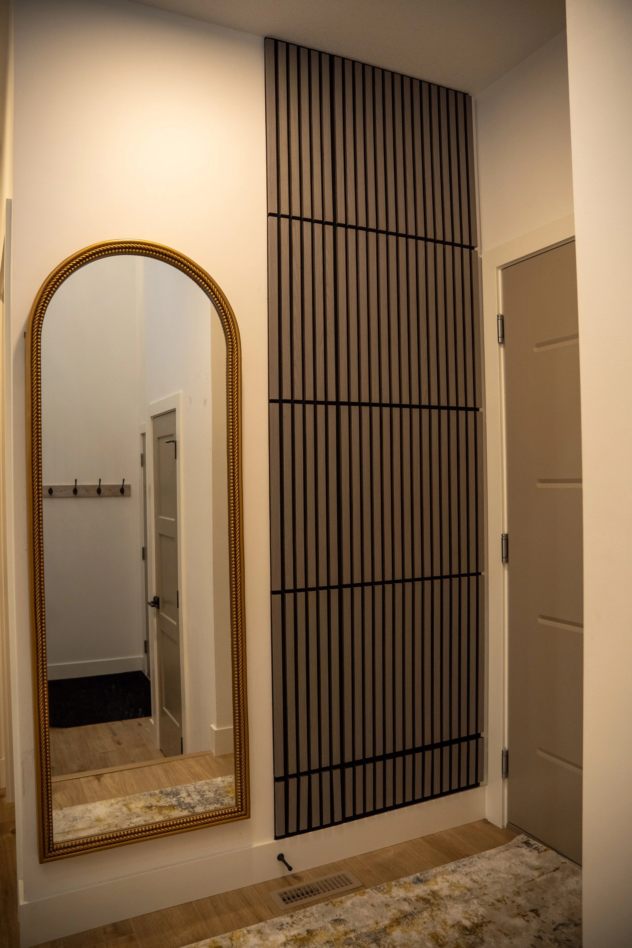 Interior hallway with a gold-framed tall mirror, a wooden louvered panel wall, a gray door, and a beige and yellow patterned rug.