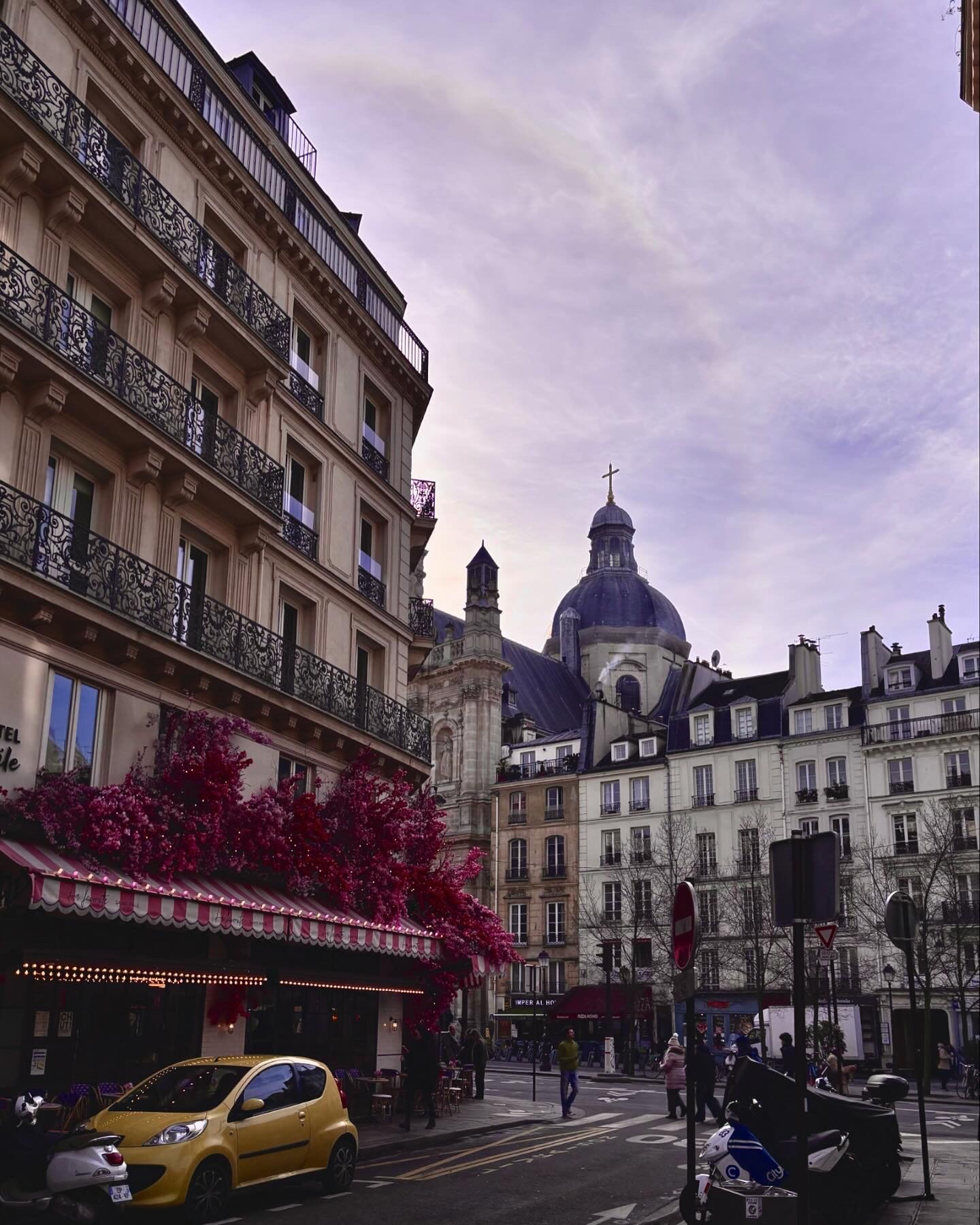 A Paris street in early spring, with a corner café, blooming flowers and a clear blue morning sky.
Eine Pariser Straßenszene im frühen Frühling, mit einem Eckcafé, blühenden Blumen und einem klaren blauen Morgenhimmel.
