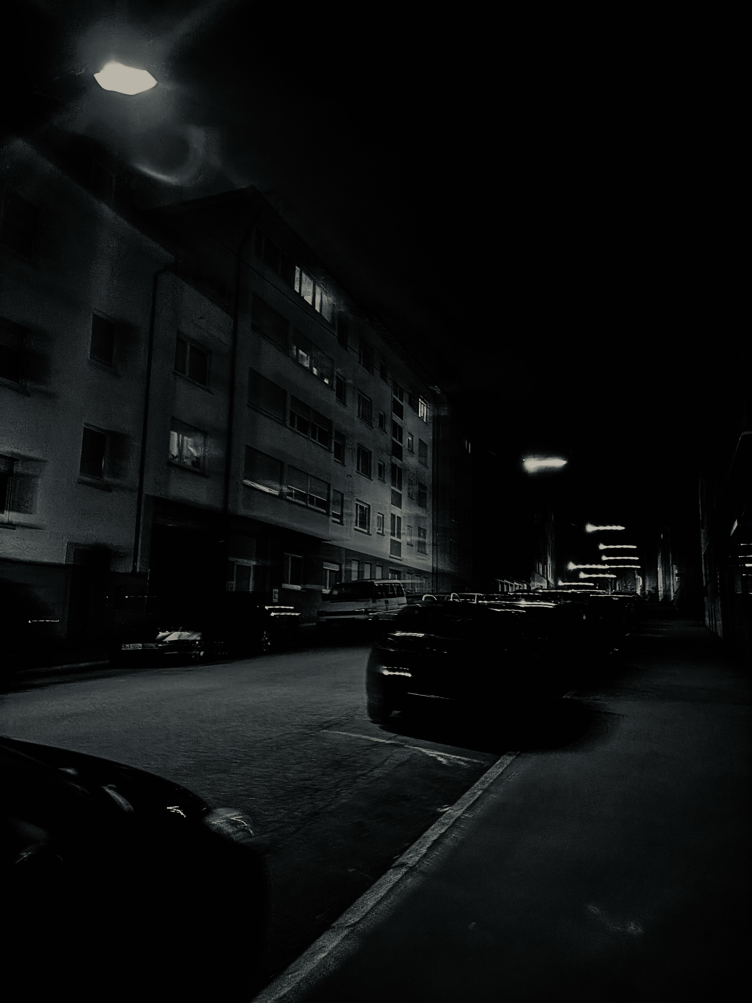 A dark nighttime street scene with wet asphalt and parked cars, capturing the quiet, moody atmosphere of the city.
Eine dunkle nächtliche Straßenszene mit nassem Asphalt und parkenden Autos, die die ruhige, stimmungsvolle Atmosphäre der Stadt einfäng