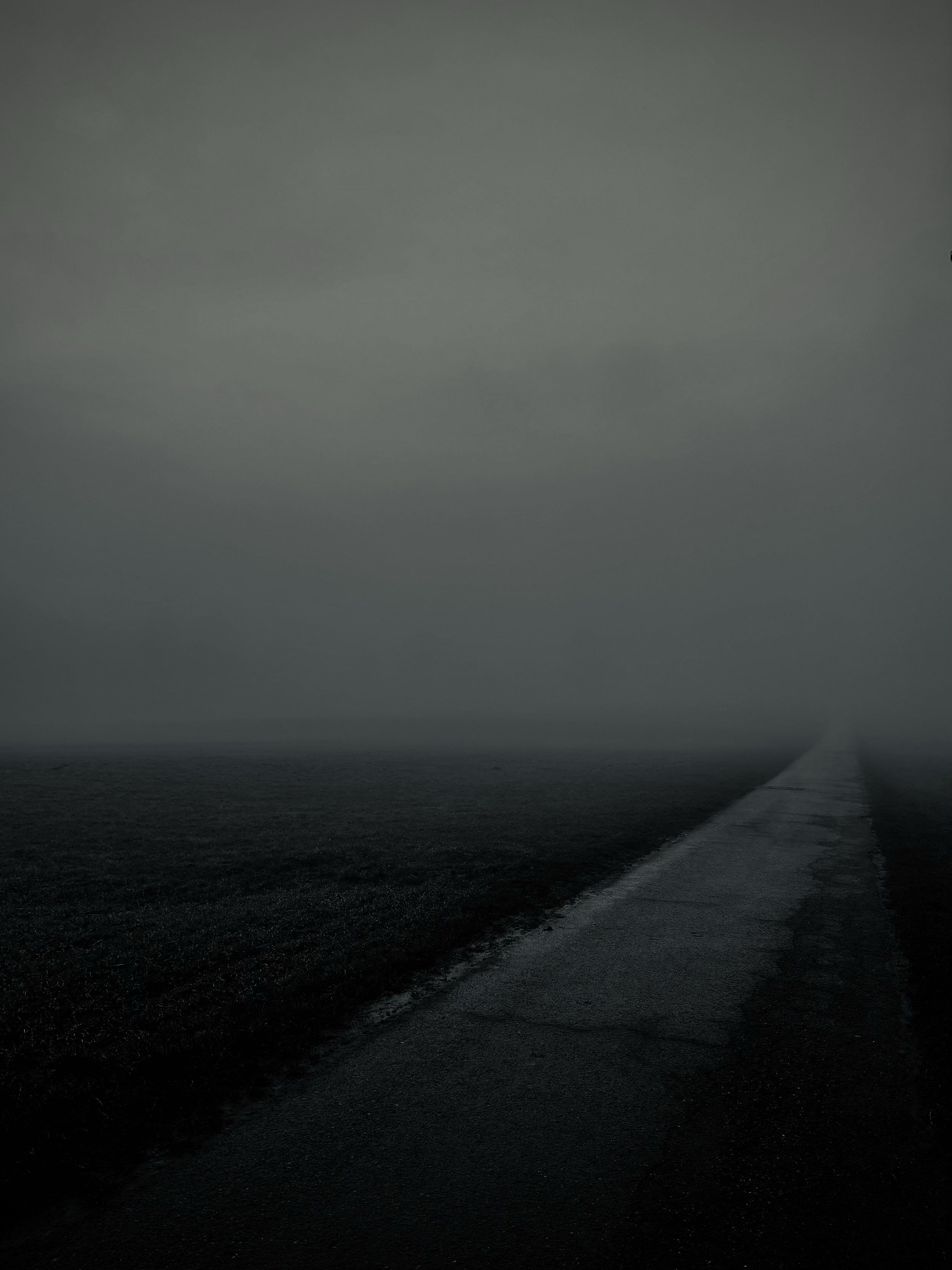 A foggy, dark road stretches into a minimal landscape, creating a moody and atmospheric scene. Eine neblige, dunkle Straße führt in eine minimalistische Landschaft und erzeugt eine stimmungsvolle, atmosphärische Szene.