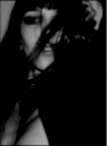 Nahaufnahme eines lachenden Gesichts, teilweise verdeckt durch dunkle Haare, in Schwarz-Weiß.