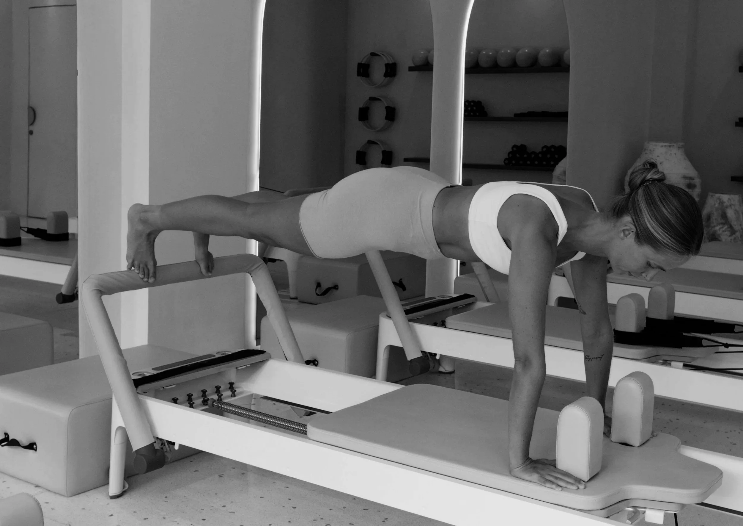 Woman performing a plank exercise on a reformer Pilates machine in a fitness studio.