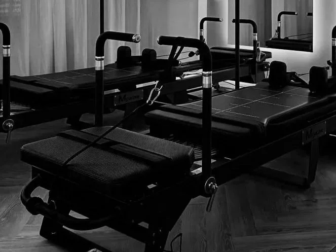 Two modern reformer machines in a fitness studio, with a mirror and curtains in the background.