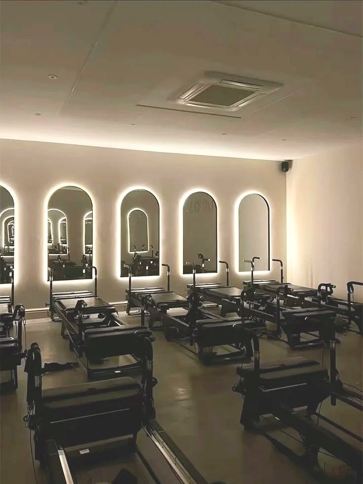 Row of Pilates reformer machines in a modern, well-lit workout studio with three large arched mirrors on the wall.