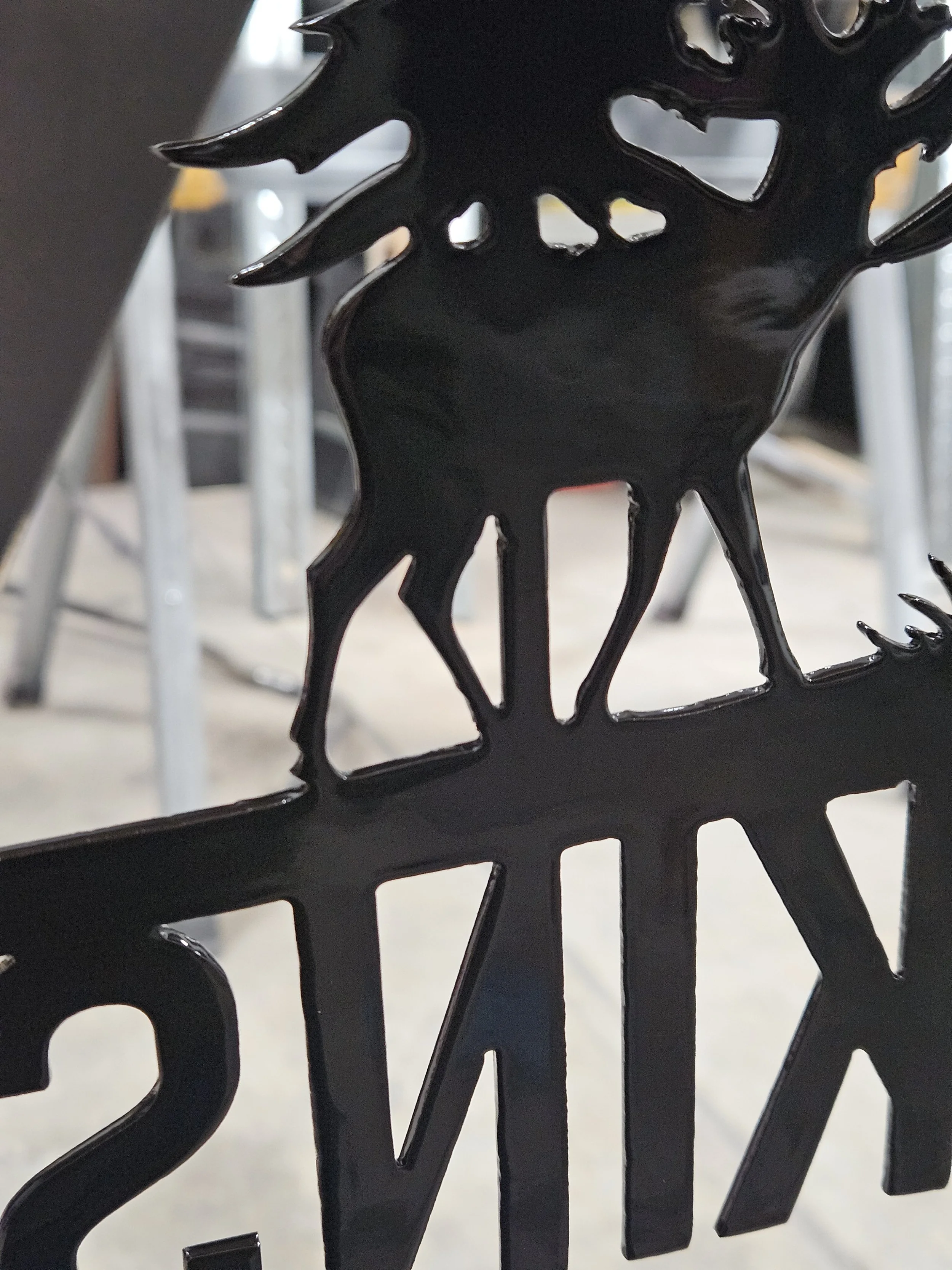 Close-up of a black metal decorative piece with cut-out designs, resembling a bird, with part of the letter 'N' visible in the background.