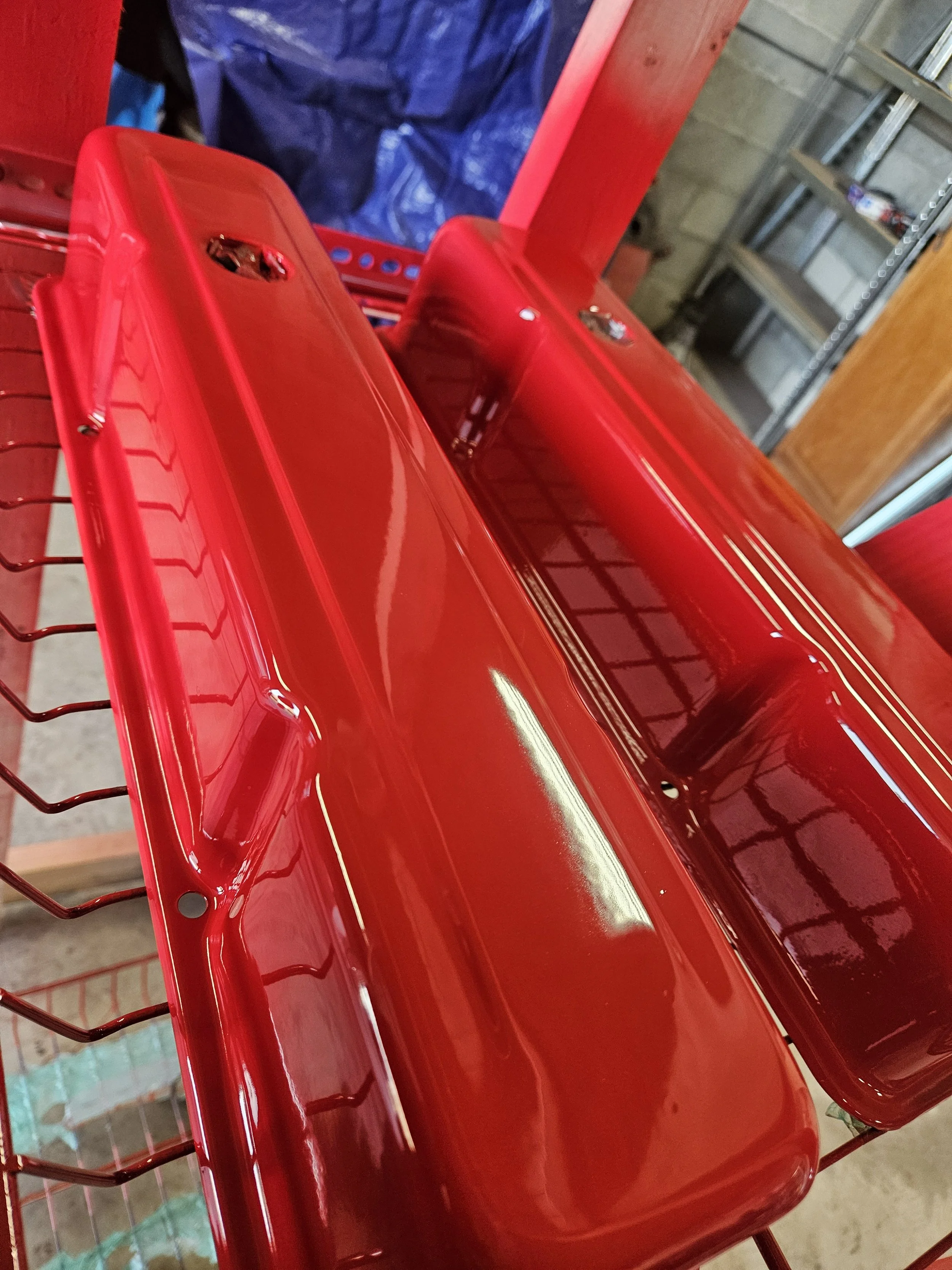 Red metal oven with glass window on top, placed on wire shelves in a workshop.