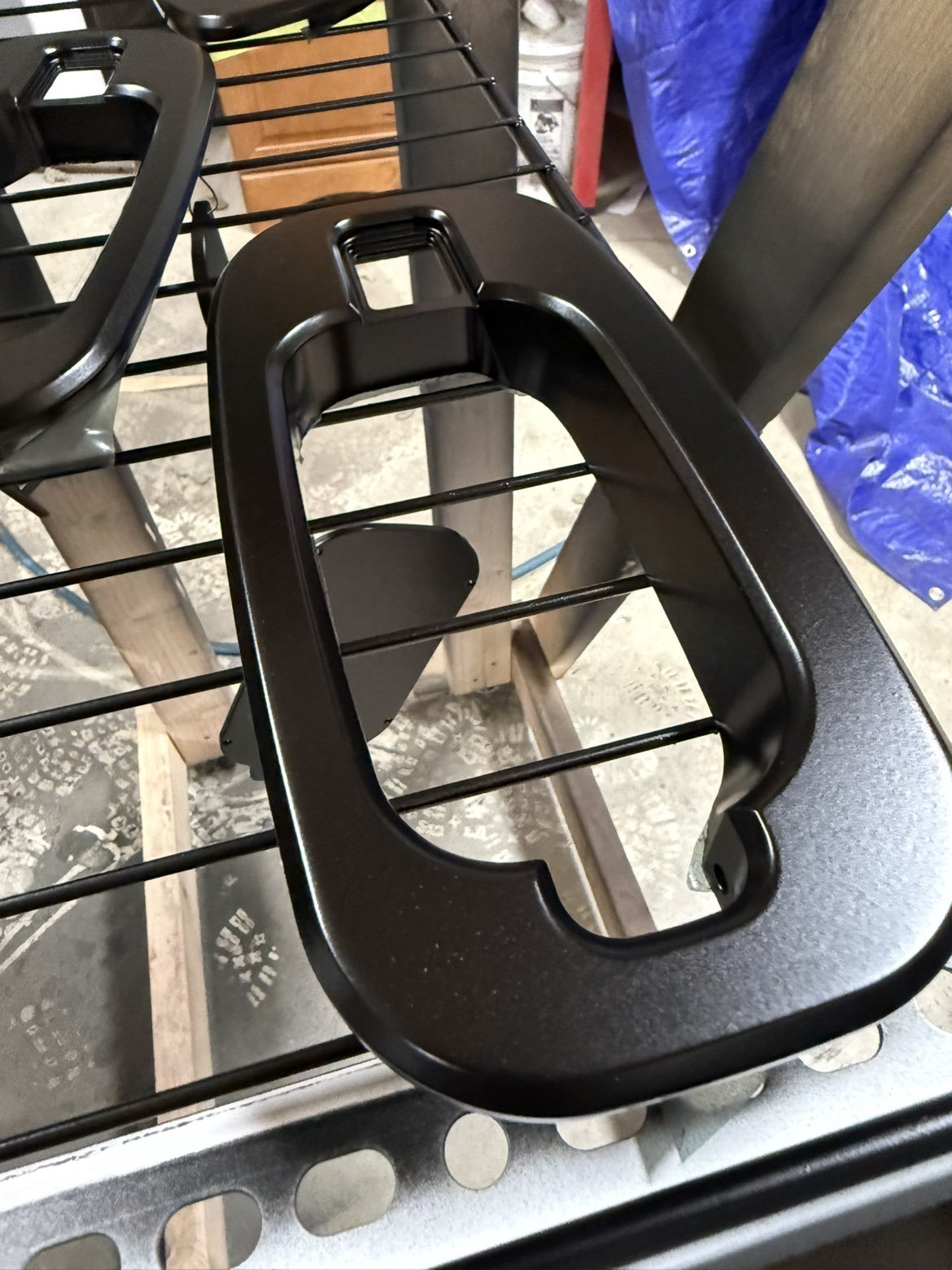 Close-up of a black plastic insert placed on a metal wire rack, possibly in a workshop or storage area.