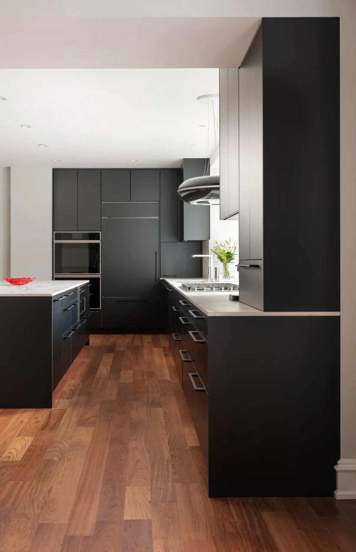 Modern kitchen with black cabinets, wooden floor, and white countertops, featuring a built-in oven and stovetop.