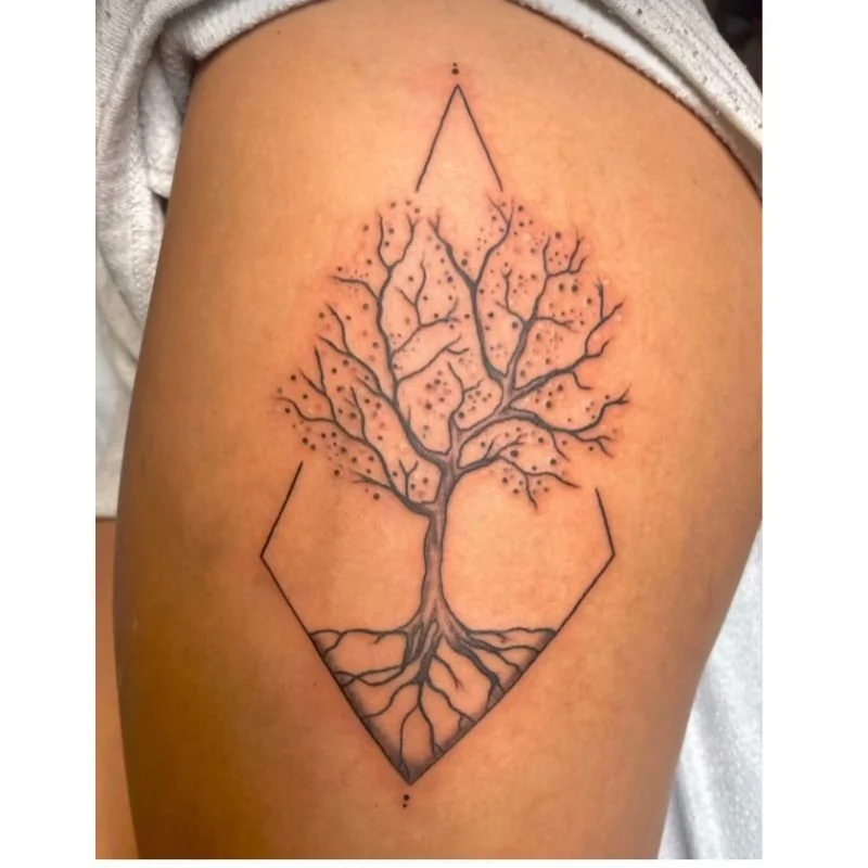 A tattoo of a tree with roots inside a diamond-shaped outline on a person's upper arm.