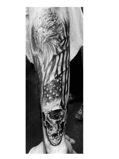 Tattoo of an eagle, American flag, and skull on a person's arm in black and white