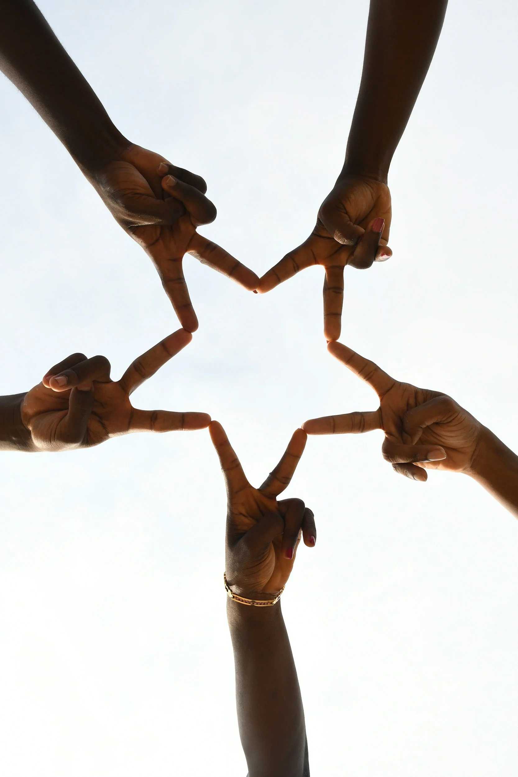 Five people making a heart shape with their hands against a light sky background.