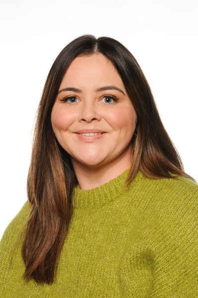 A woman with long brown hair wearing a green sweater, smiling at the camera against a plain white background.
