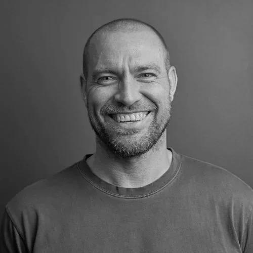 Black and white portrait of a smiling man with a beard and short hair, wearing a casual shirt.