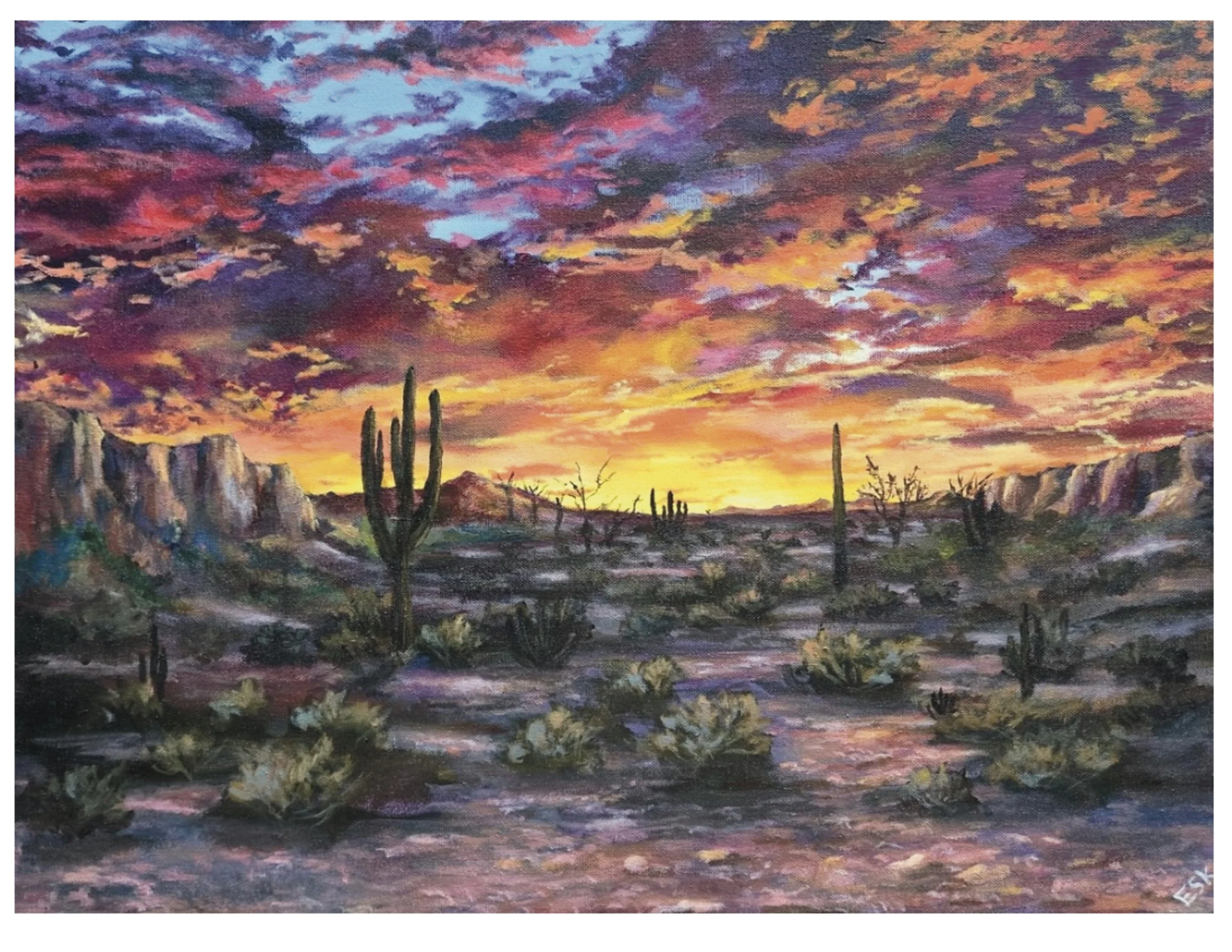 A desert landscape at sunset with colorful sky, cacti, arid terrain, and distant mountains.