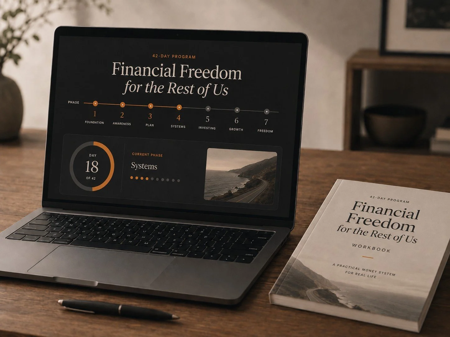 A laptop displaying a financial freedom program with a progress tracker for the 42-day course, and a workbook titled 'Financial Freedom for the Rest of Us' on a wooden desk. There is also a black pen in front of the laptop.