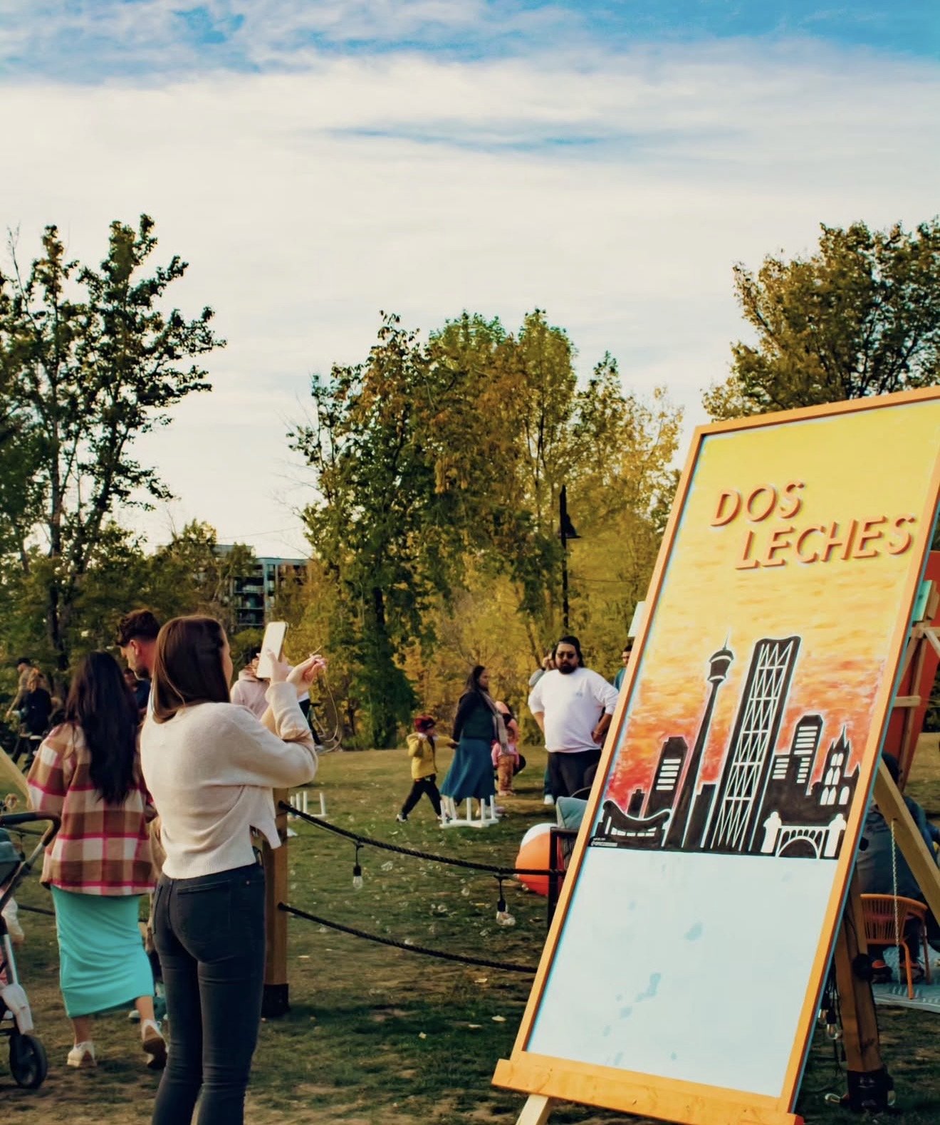 Attendees at a Dos Leches free community event in a Calgary park with Dos Leches signage
