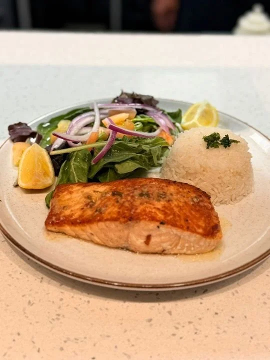 A plate of cooked salmon with a side of mixed salad and a mound of rice garnished with parsley, on a white table.