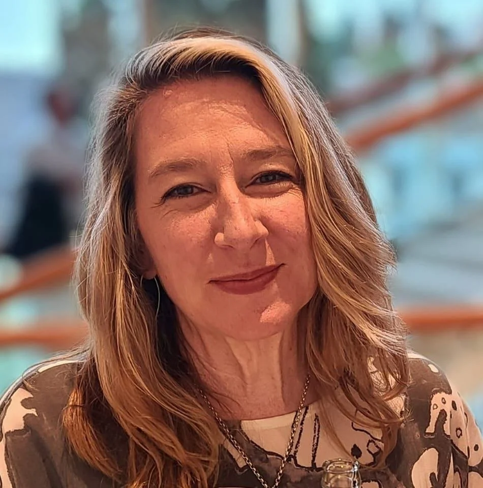 A woman with shoulder-length reddish-brown hair smiling in a blurred background.