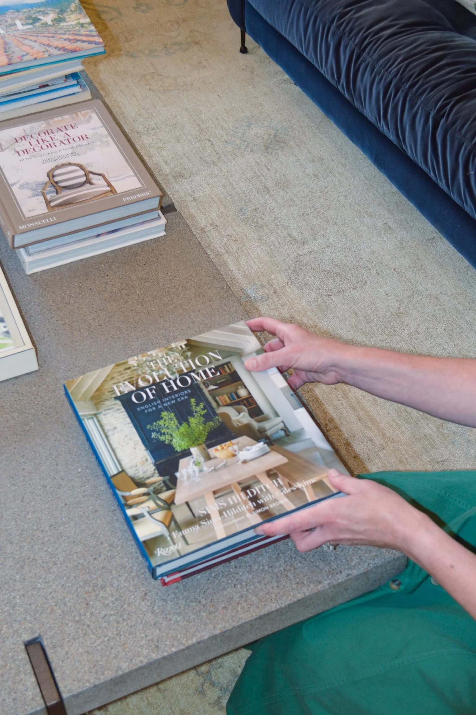 Person holding a large home decoration and interior design book while browsing nearby books on a table.