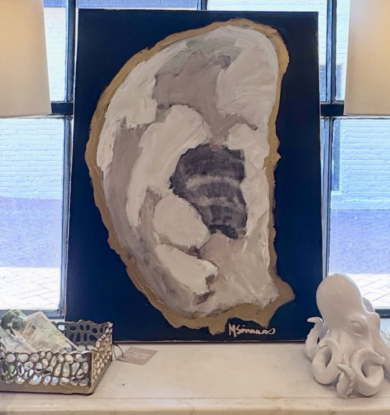 Abstract painting of a human ear on a dark background, signed by M. Simmons, placed on a white surface beside a white octopus-shaped sculpture and a metallic basket.