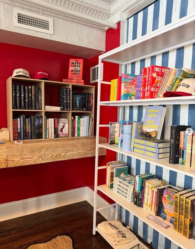 Bookshelves filled with books, some hats on top, in a room with red and blue striped wallpaper and a red wall.