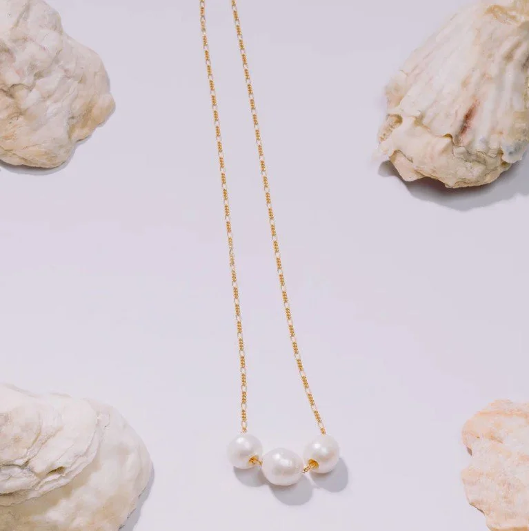Gold chain necklace with four large white pearls, surrounded by four rocks on a white background.