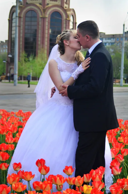 A bride and groom kissing in a field of red tulips with a large church building in the background.