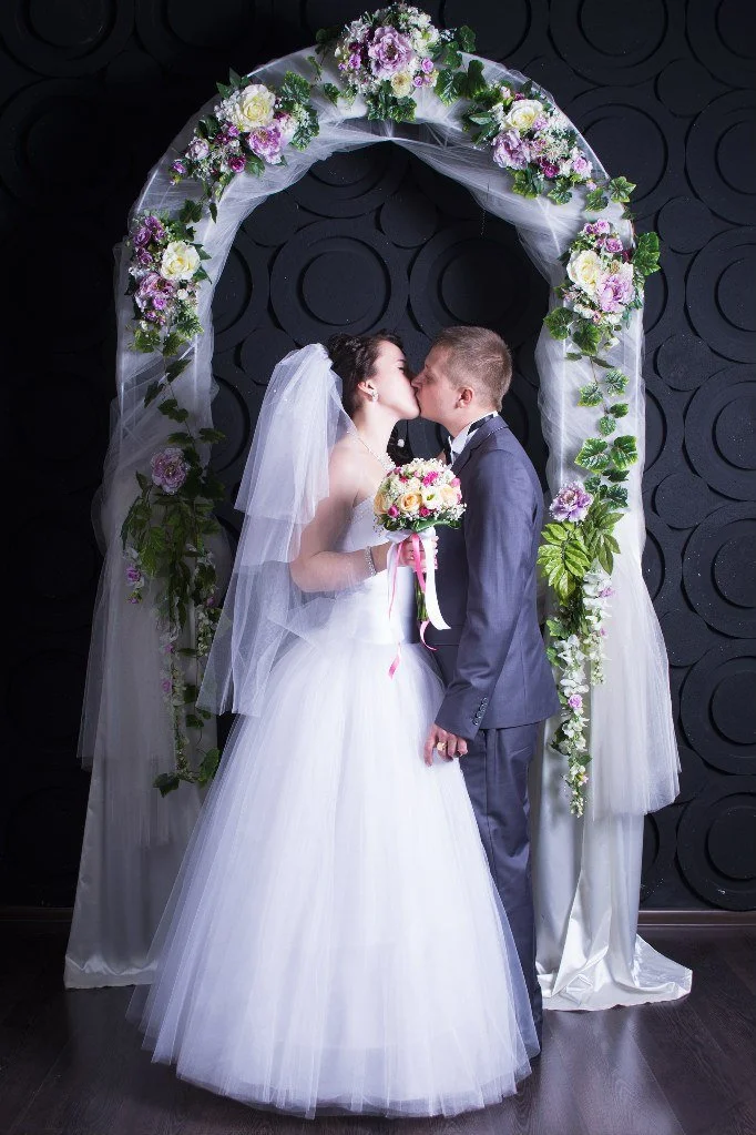 Bride and groom kissing under a floral arch on their wedding day.