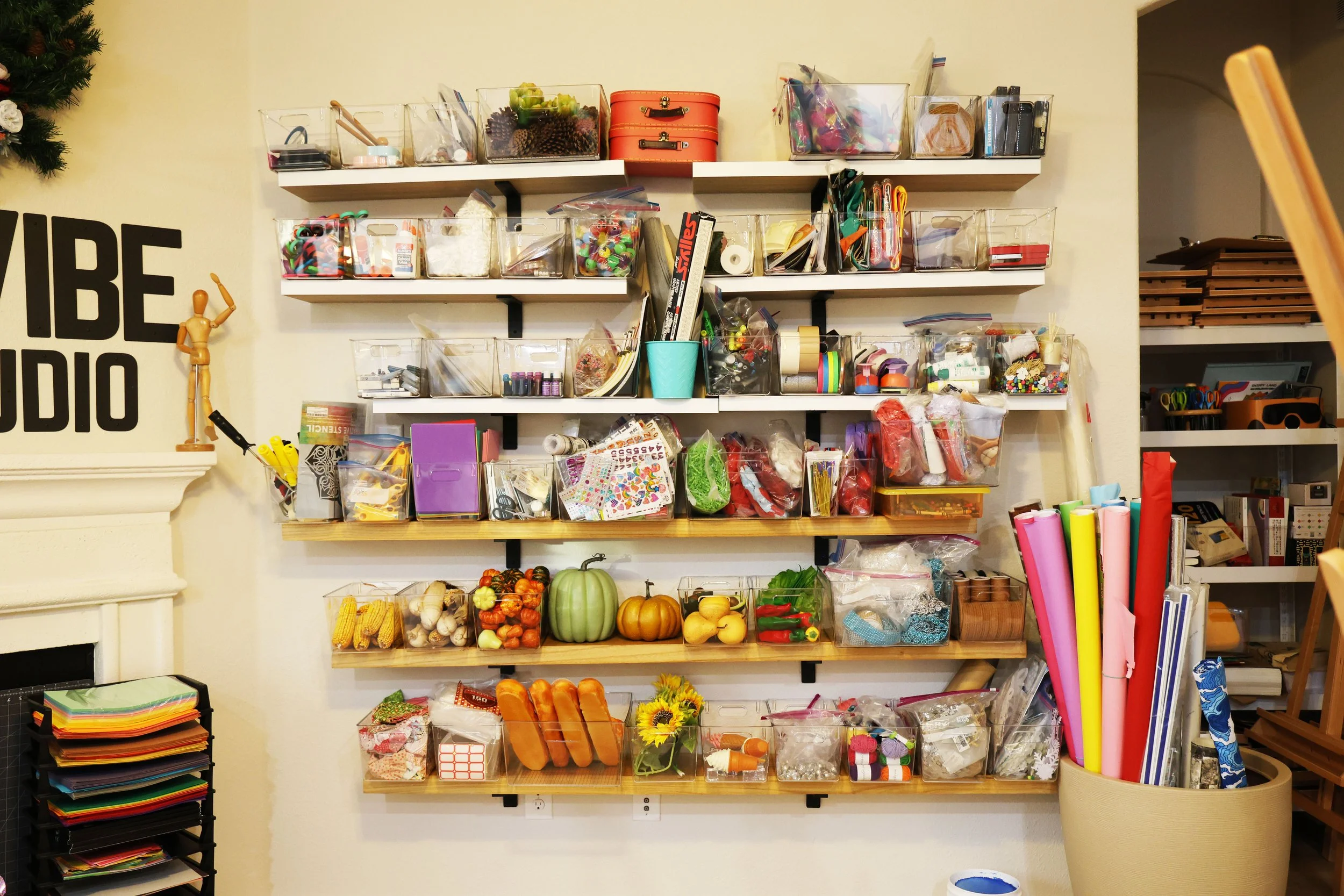 Wall with multiple shelves holding craft supplies, toys, and decorations in a creative studio.