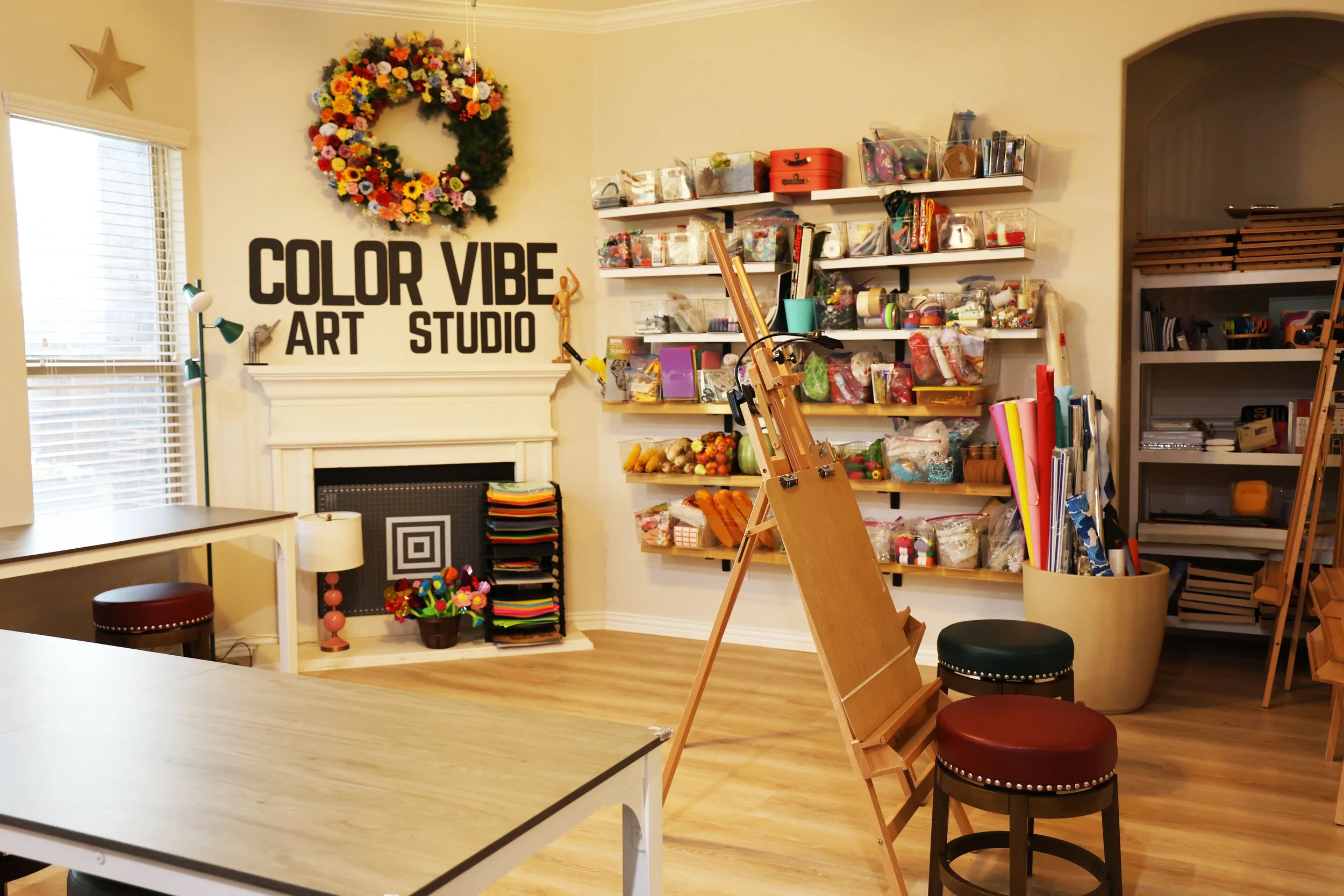 Interior of an art studio named 'Color Vibe Art Studio' with shelves filled with art supplies, an easel, a table, and seating.