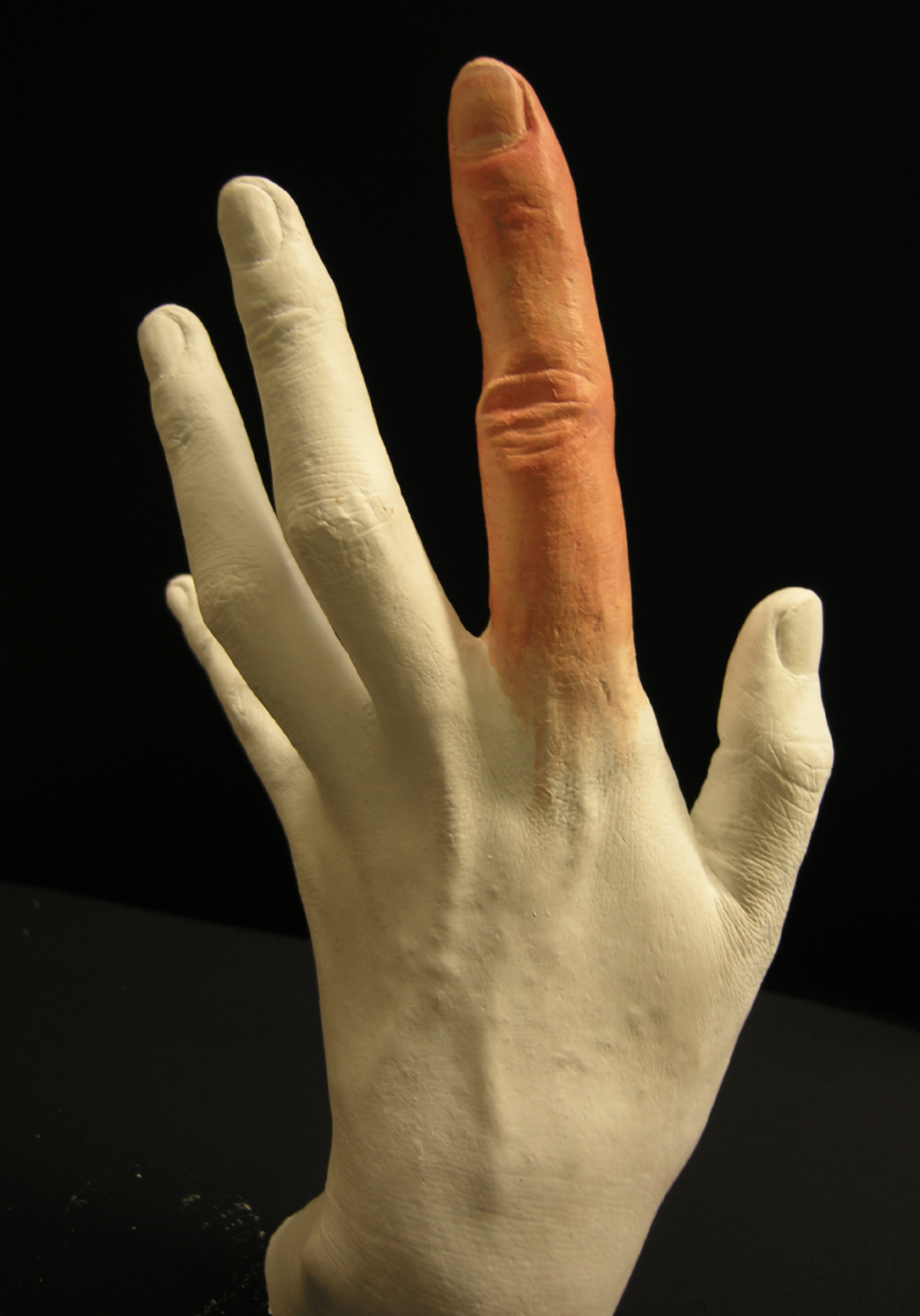 A ceramic or plastic hand model with the middle finger painted orange, set against a black background.