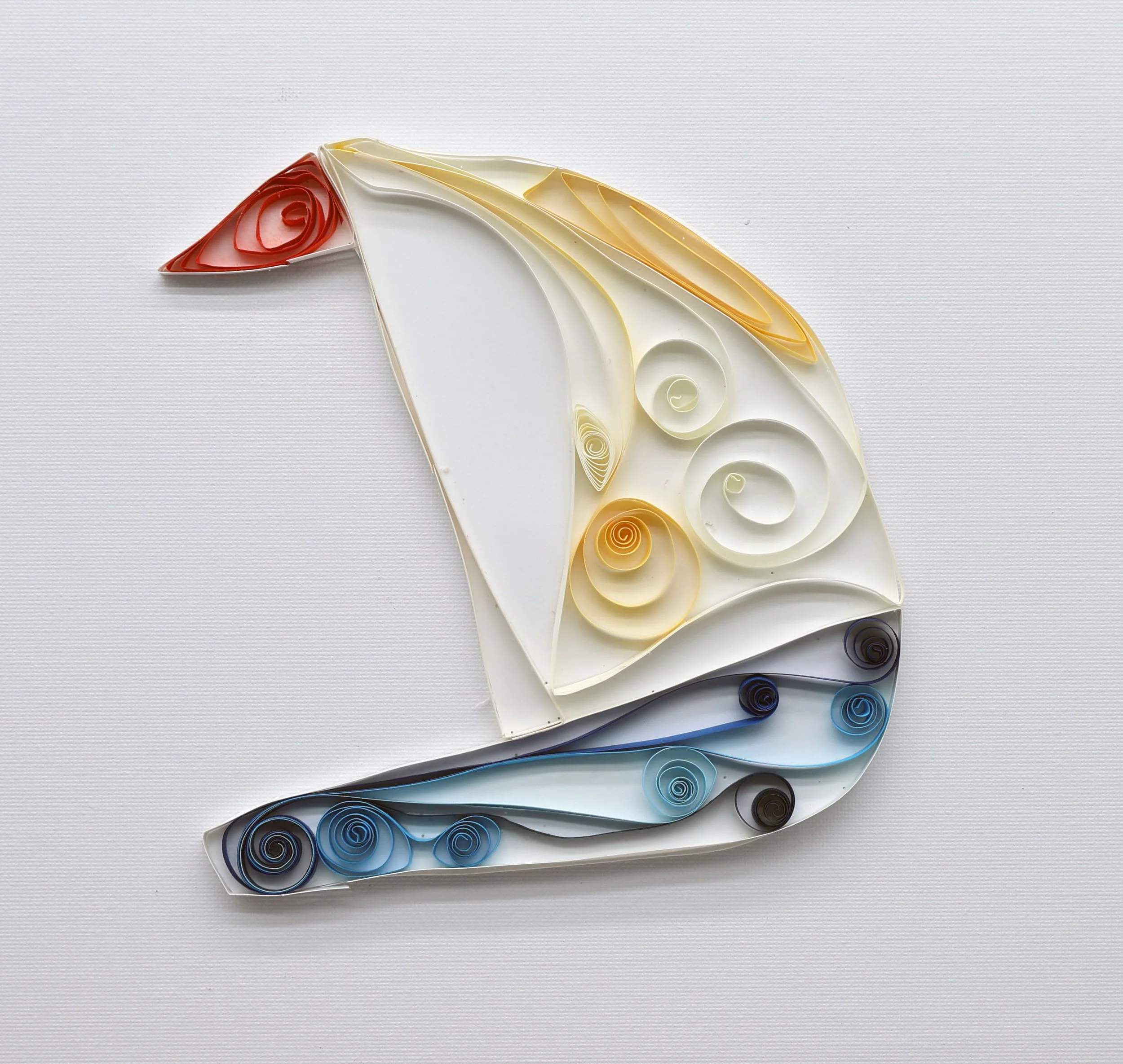 Quilled paper art of a sailboat with a red sail, yellow and white body, and blue waves.