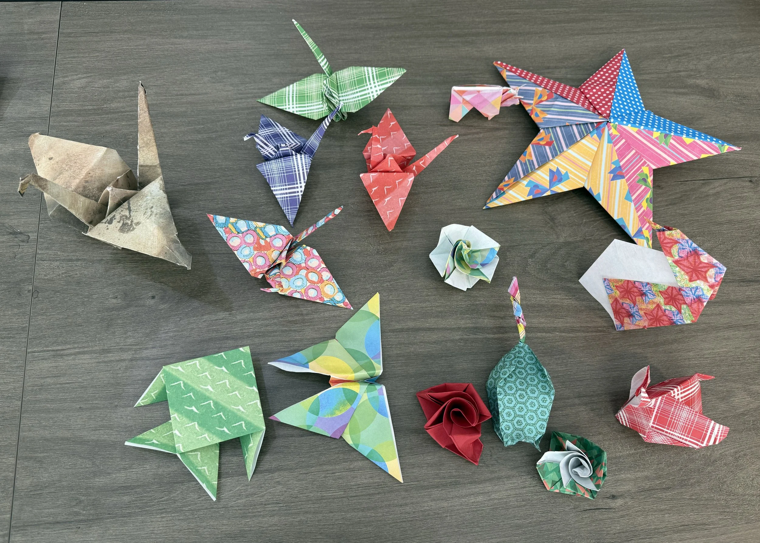 Various colorful origami paper cranes and flowers laid out on a wooden surface.