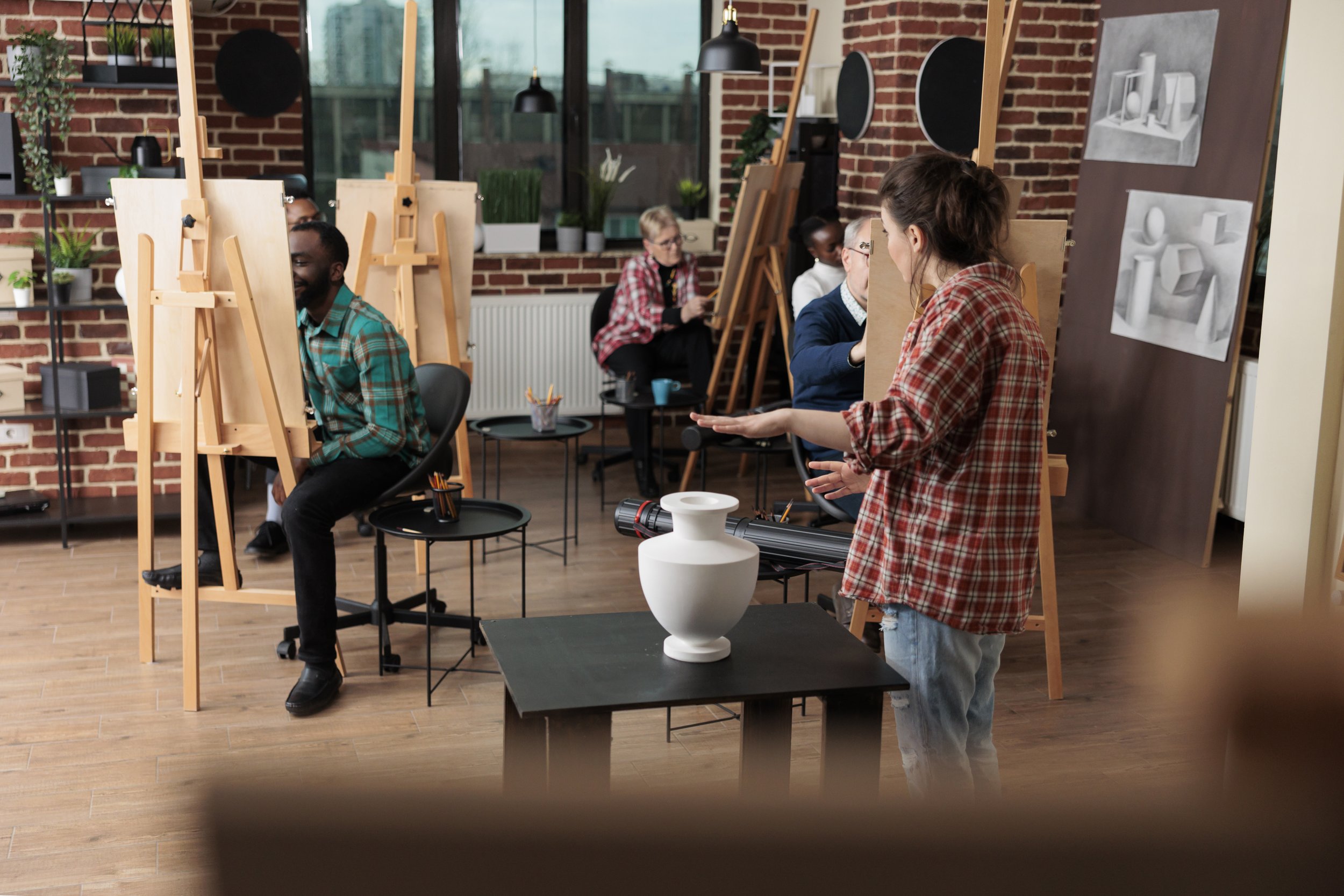 Group of people painting and drawing in an art studio with easels, artwork, and plants.