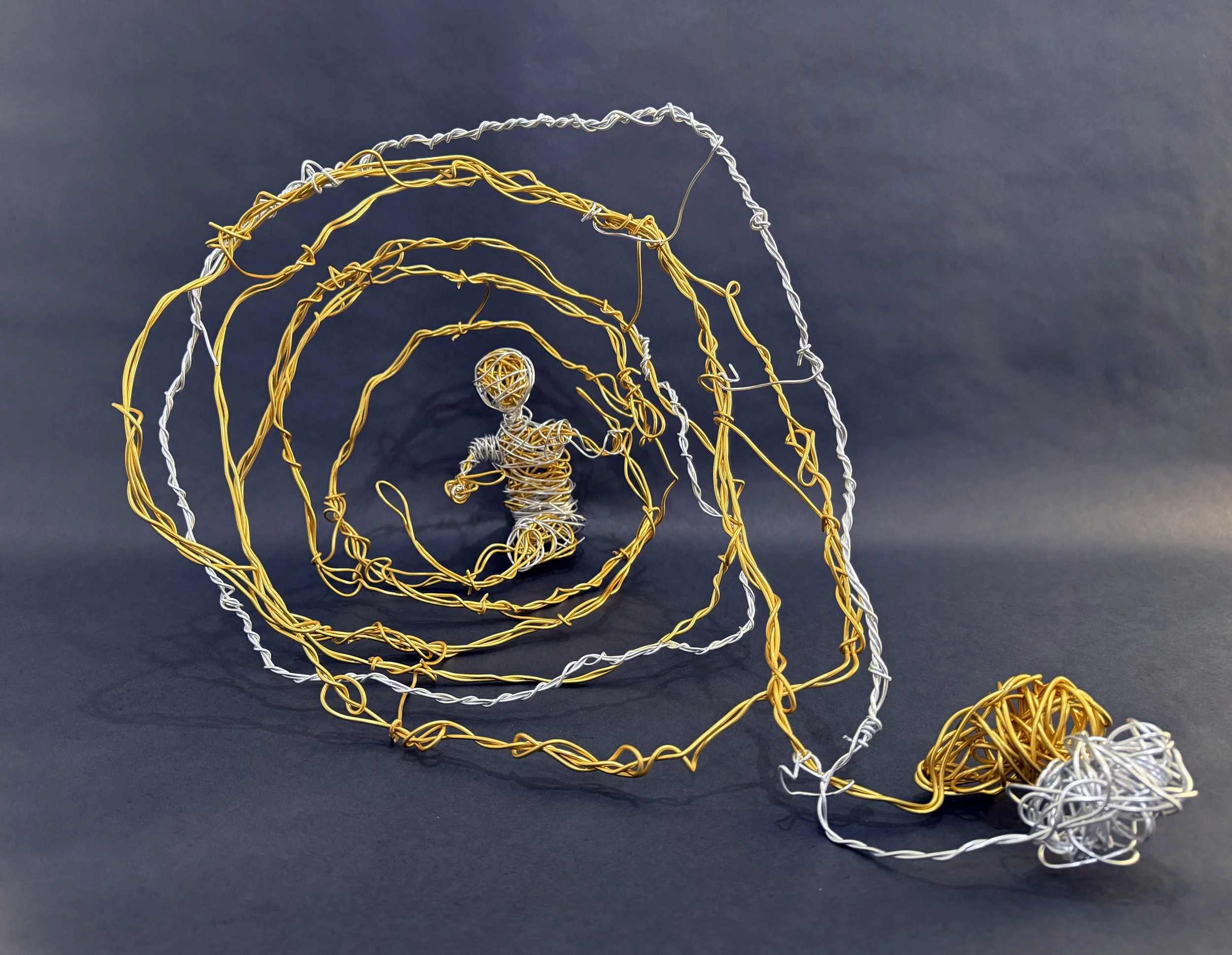Wire sculpture of a child running through a tunnel of yellow and silver wires, with a pile of tangled wires at the end.