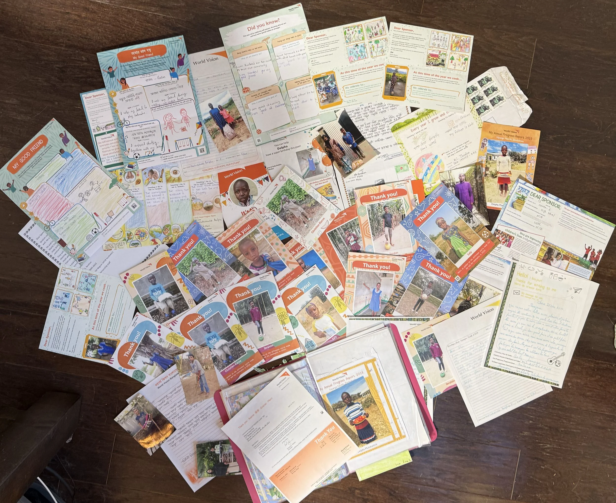 A collection of letters, thank you notes, and photo cards, some featuring children, laid out on a wooden floor.